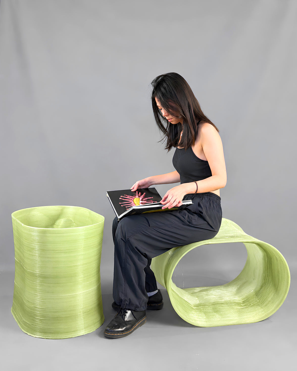 Woman seated on a translucent green 3D-printed bench beside a matching side table from the After the Last Sip collection.