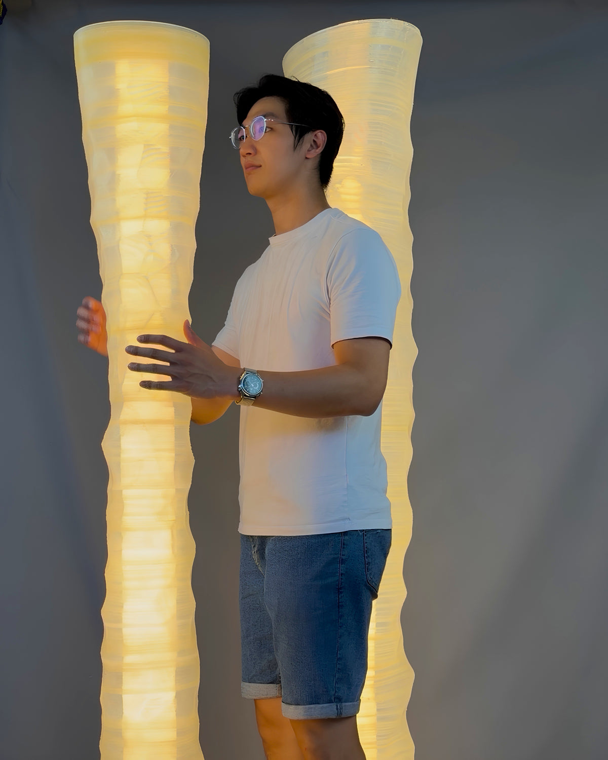 Designer Chao-Chun Kung standing between two illuminated, large-scale 3D-printed lamps created for After the Last Sip.