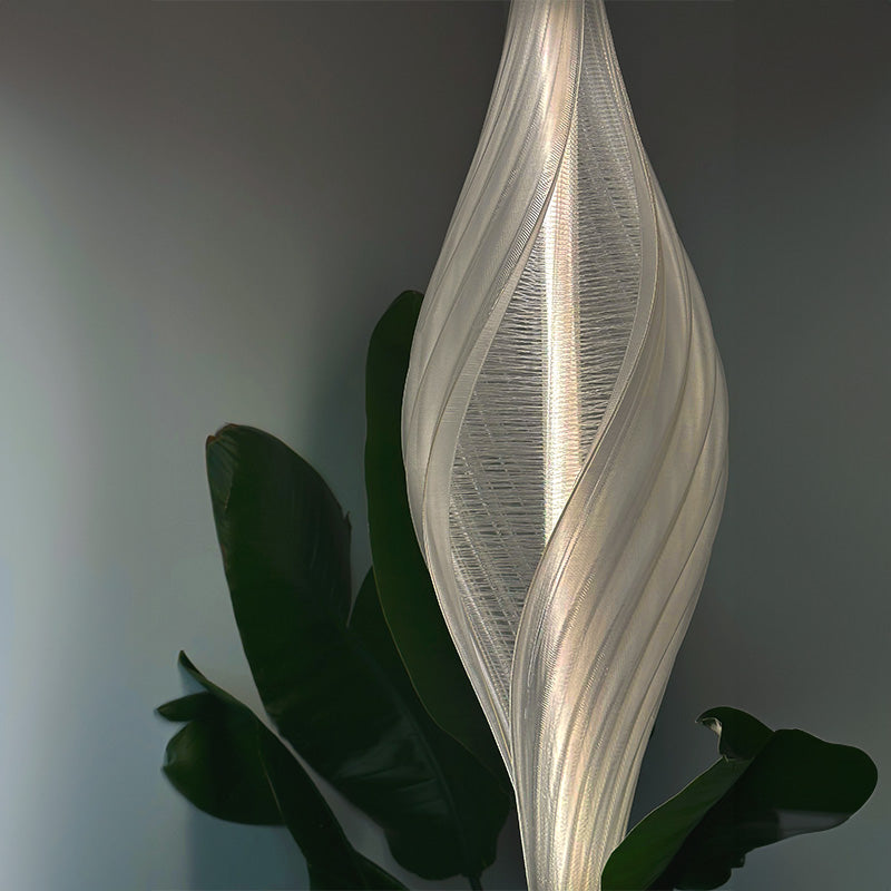 Pupa Mandala Clear Lamp glowing beside dark green foliage, original product photograph used in the Pupa lighting campaign.